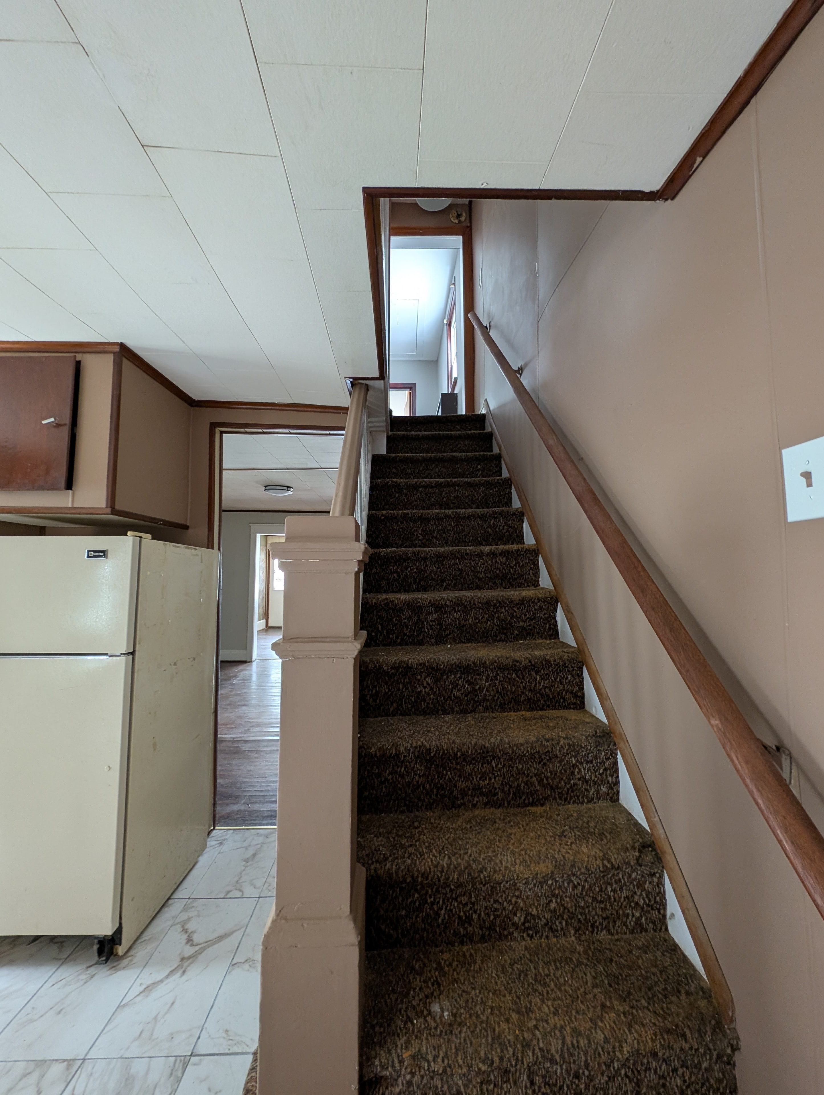 Carpeted staircase with wood railing next to kitchen