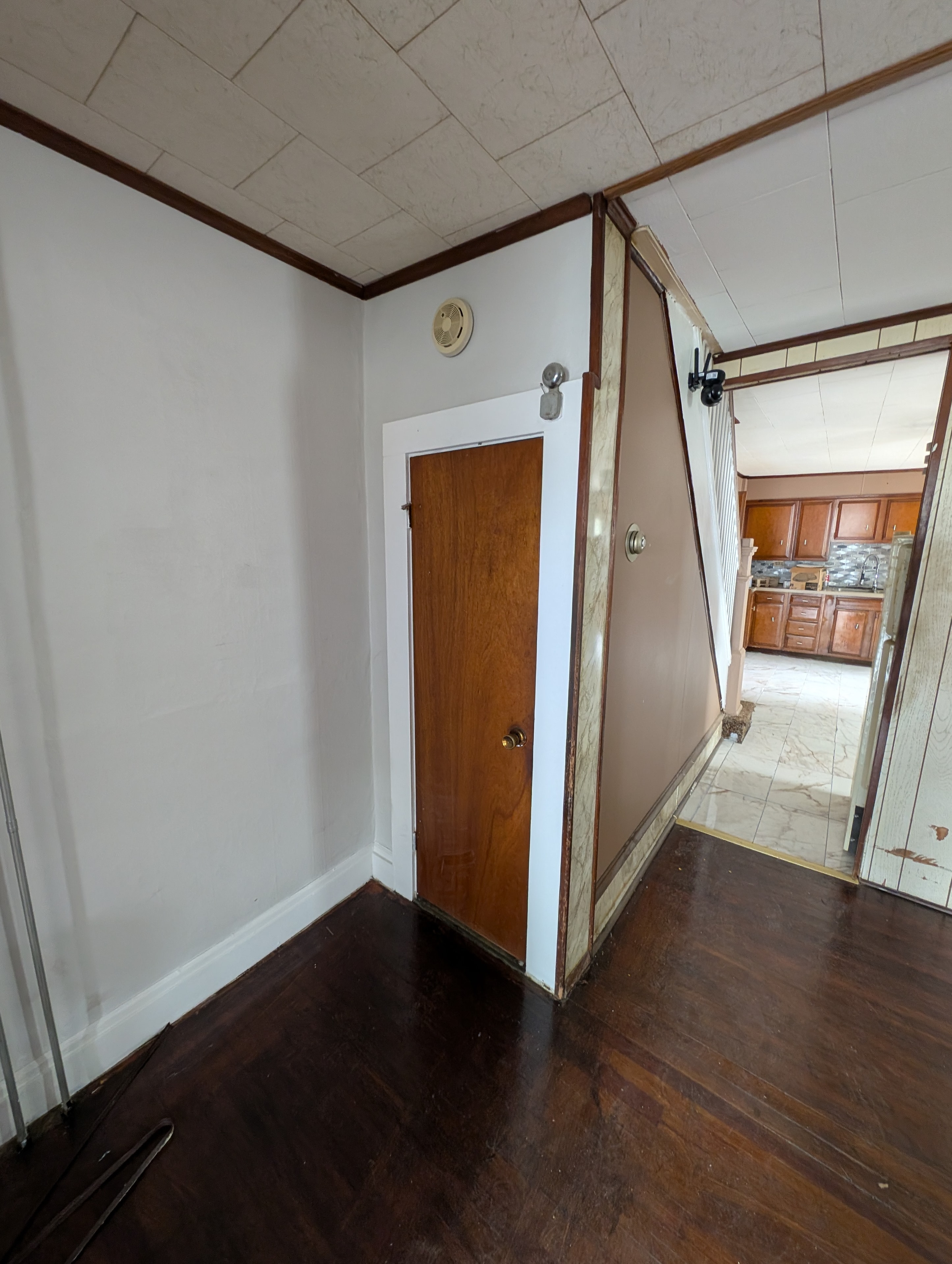 Hallway with wood door, dark floors, and view into kitchen