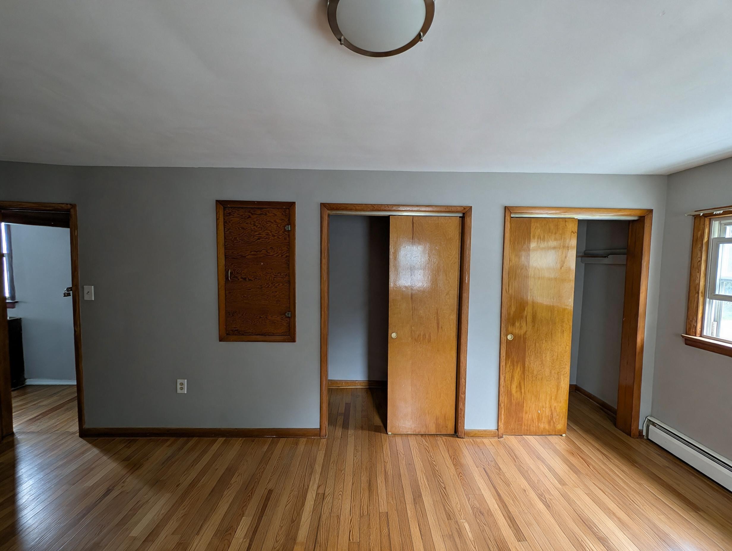 Bedroom with gray walls, multiple wood doors and closets, and hardwood floors
