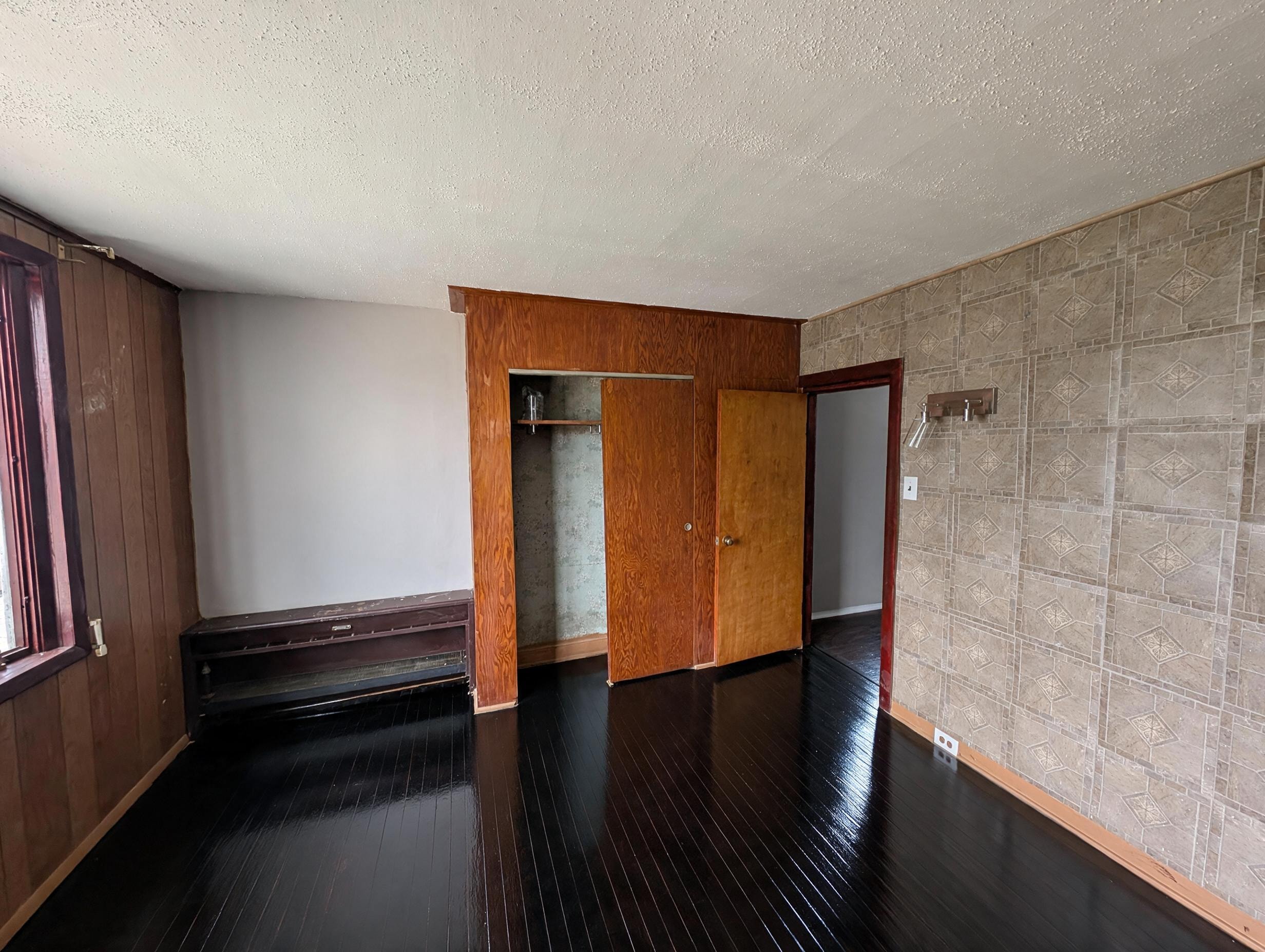 Bedroom with dark floors, open closet, tile accent wall, and wood paneling