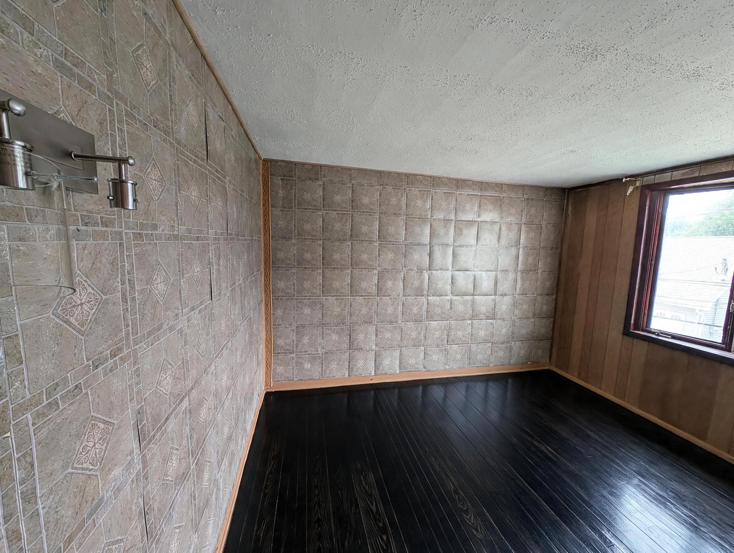 Bedroom corner with patterned tile walls, dark hardwood floors, and window