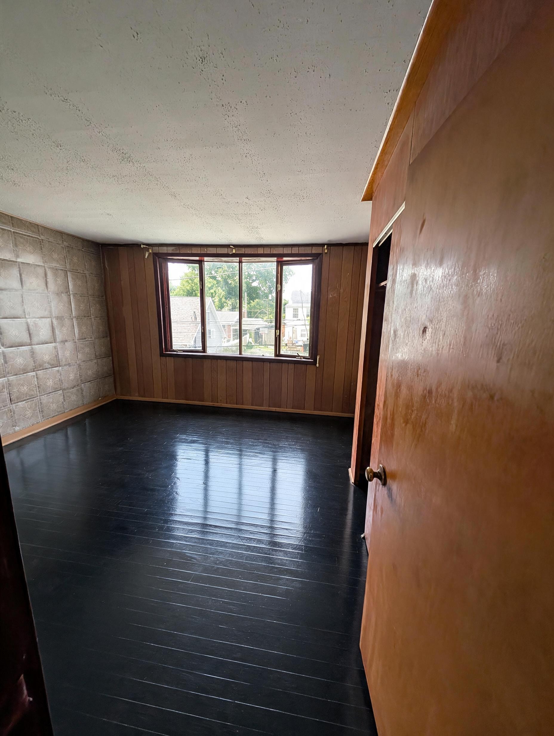 Room with wood paneling, tile accent wall, dark floors, and large window
