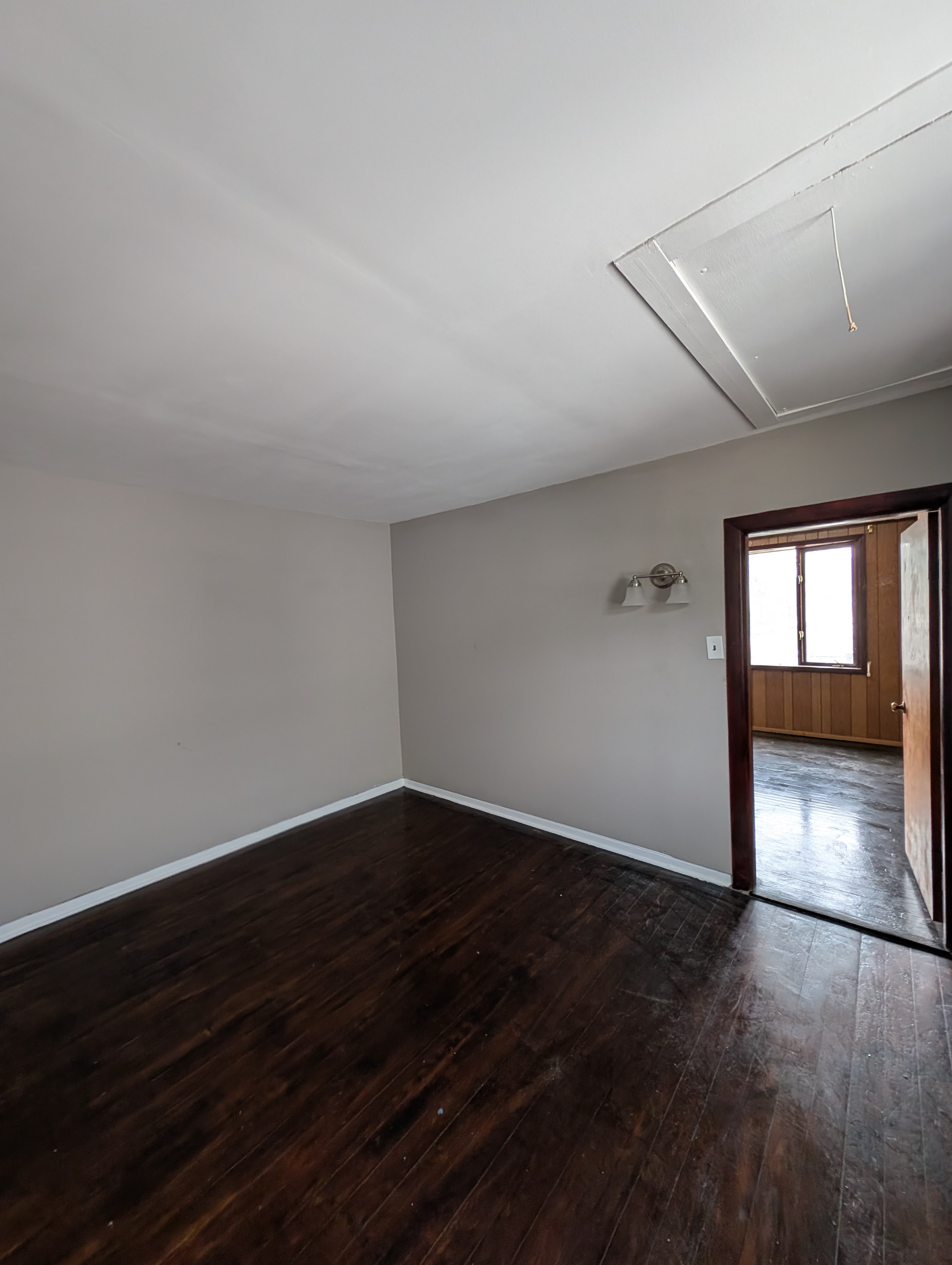 Gray-walled room with dark hardwood floors, wall sconce, and doorway to adjacent room