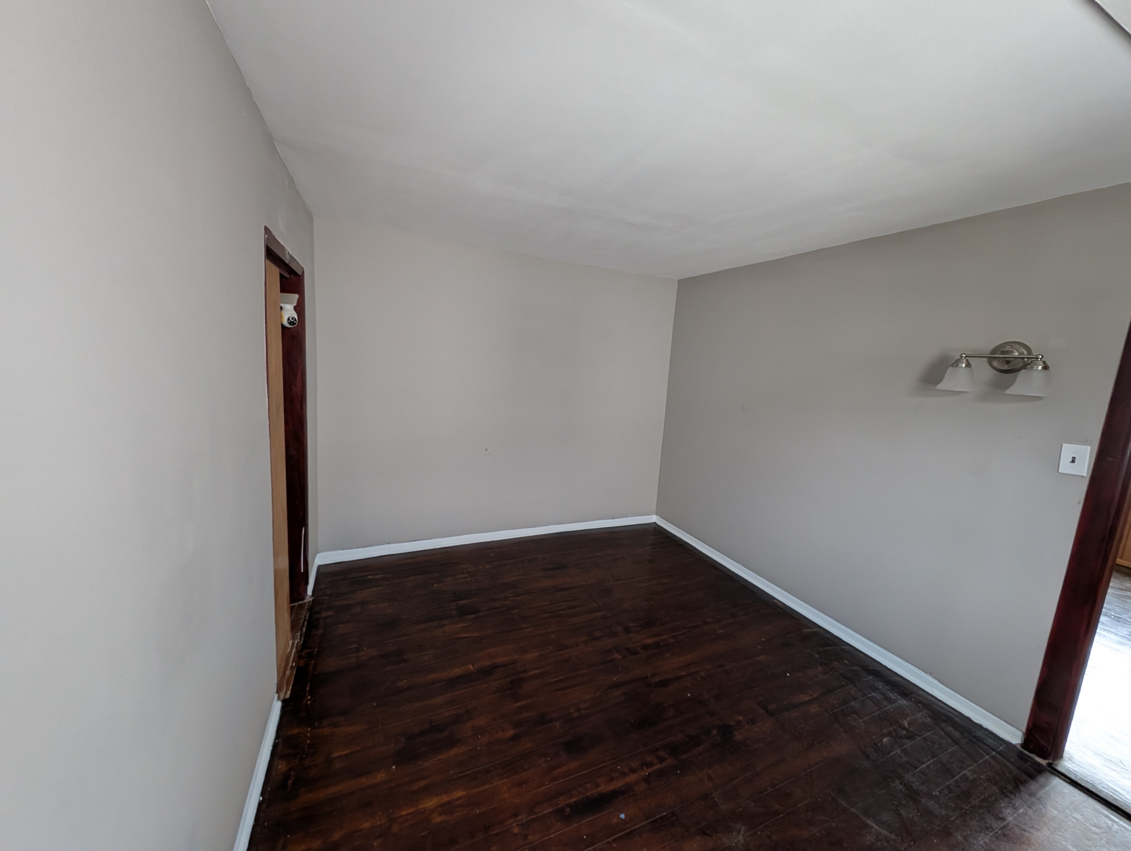 Gray-walled room with dark hardwood floors, wall sconce, and two doorways